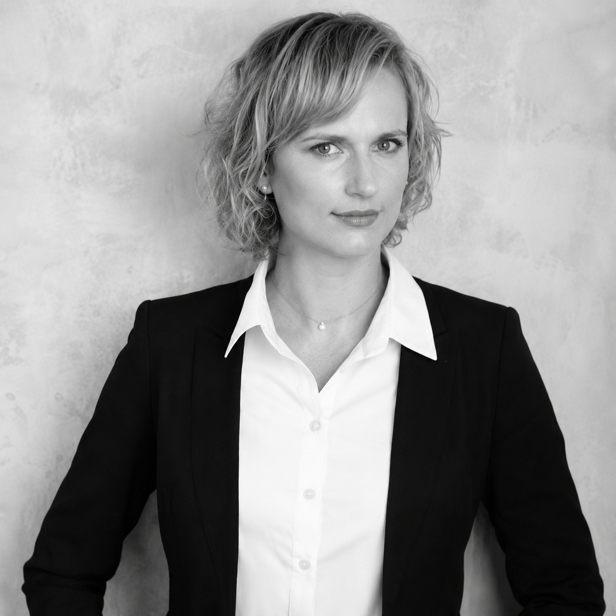 Black and white portrait of a woman with curly short hair wearing a black blazer and white shirt, looking confidently at the camera.
