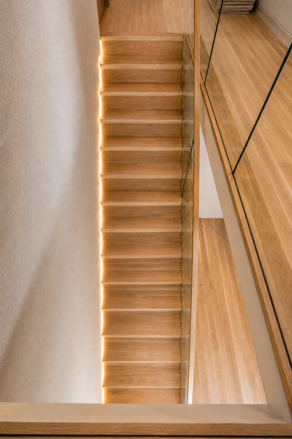Wooden staircase with glass railing and LED lighting at the edge, viewed from below in a modern interior.