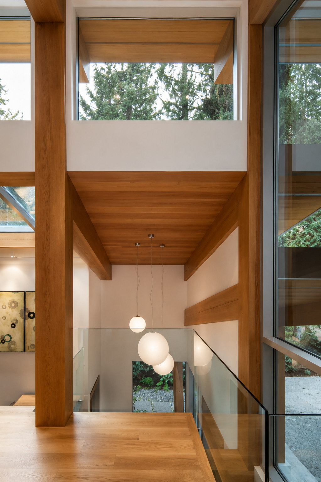Interior view of a modern house with wooden beams, large glass windows, a wooden ceiling, and hanging pendant lights.