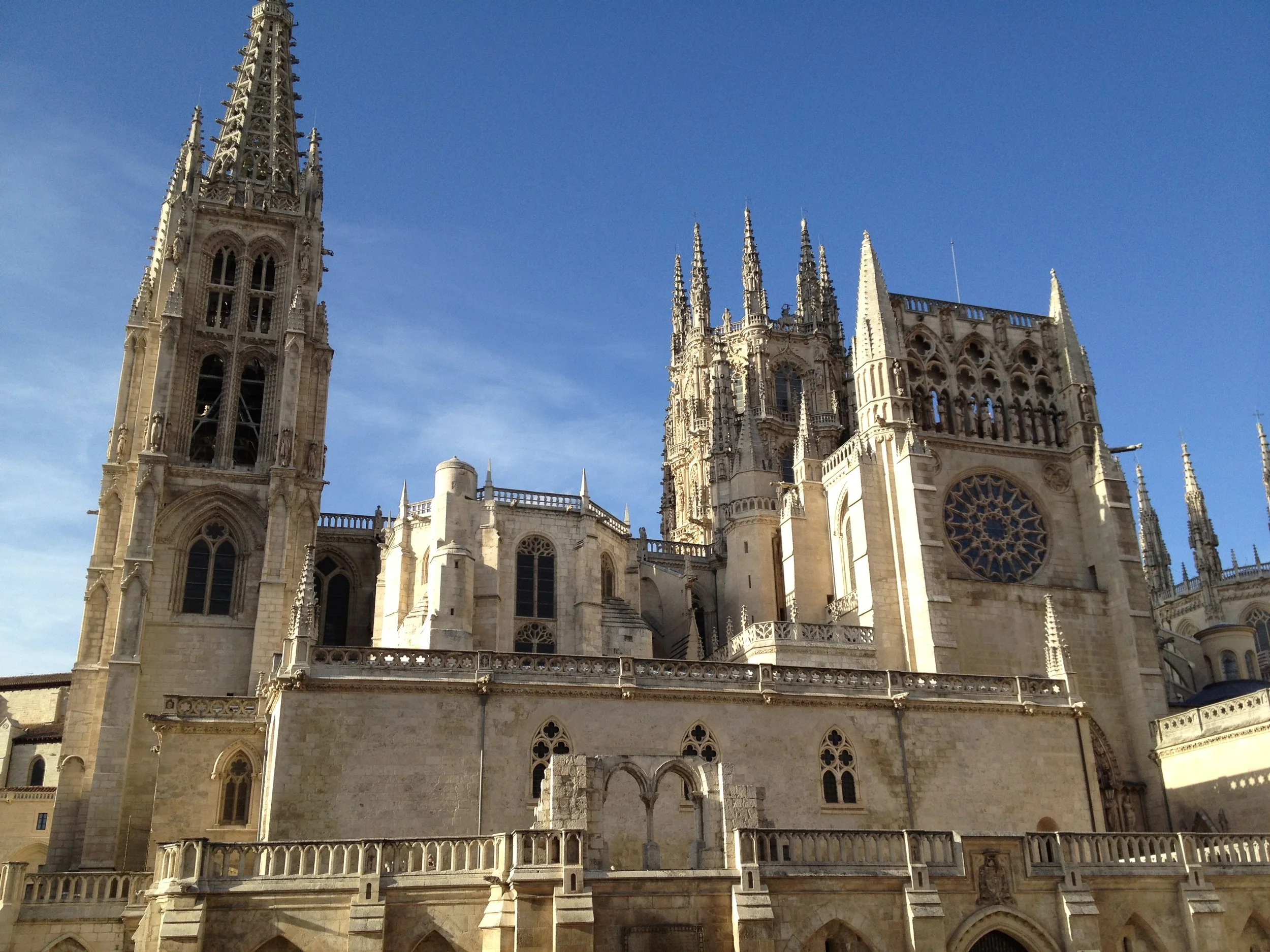 Gothic cathedral with tall spires and intricate stone carvings, featuring large stained glass windows and a detailed facade, set against a clear blue sky.