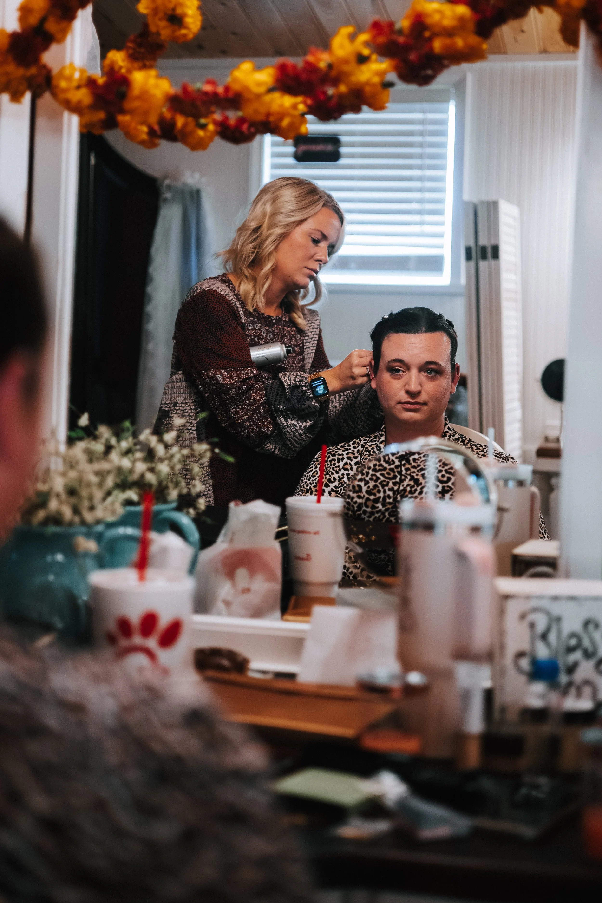 A woman getting her hair styled in a salon, with various cups and fast food items on a table in the foreground.