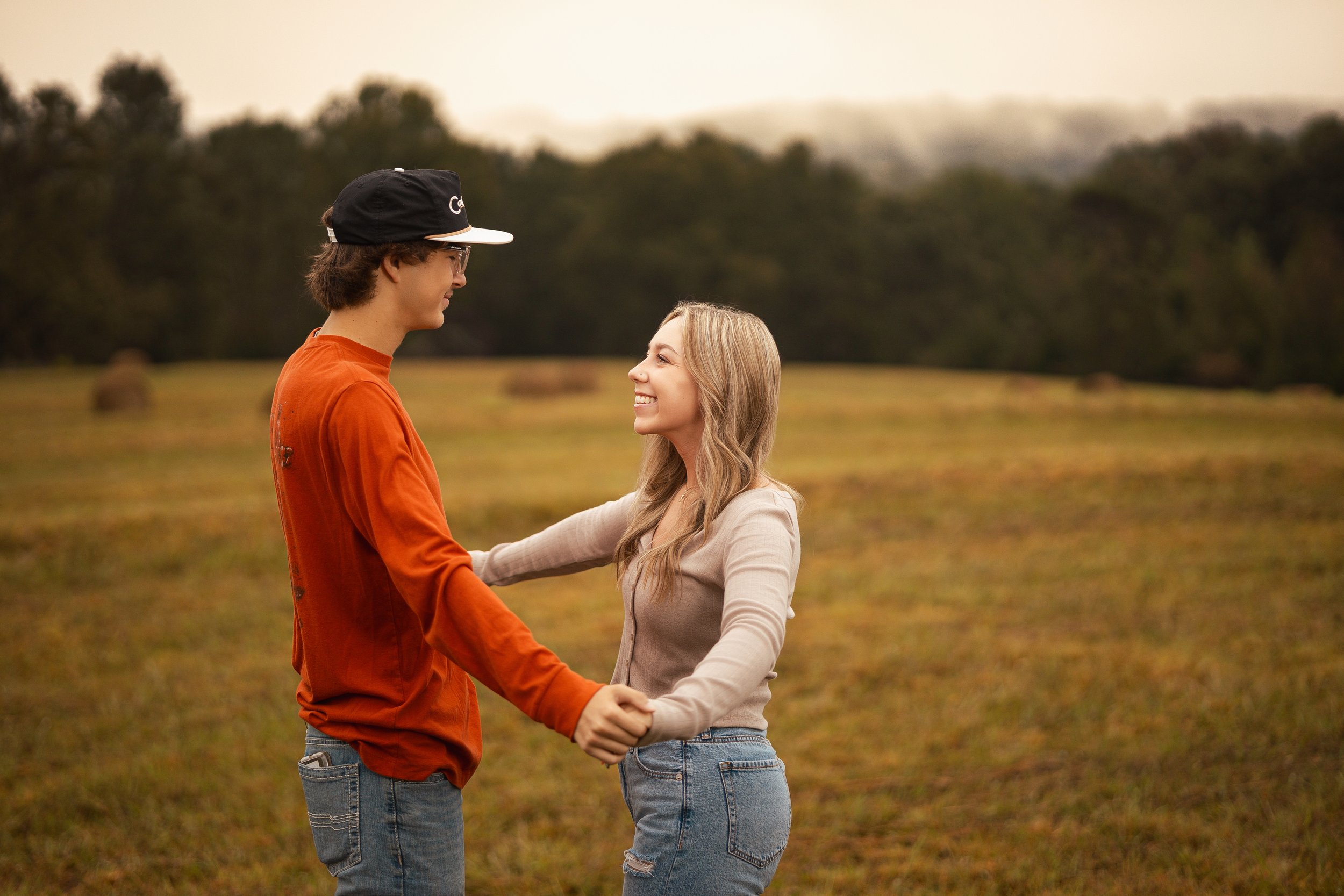 A young couple holding hands and enjoying a moment together outdoors in a field during sunset.