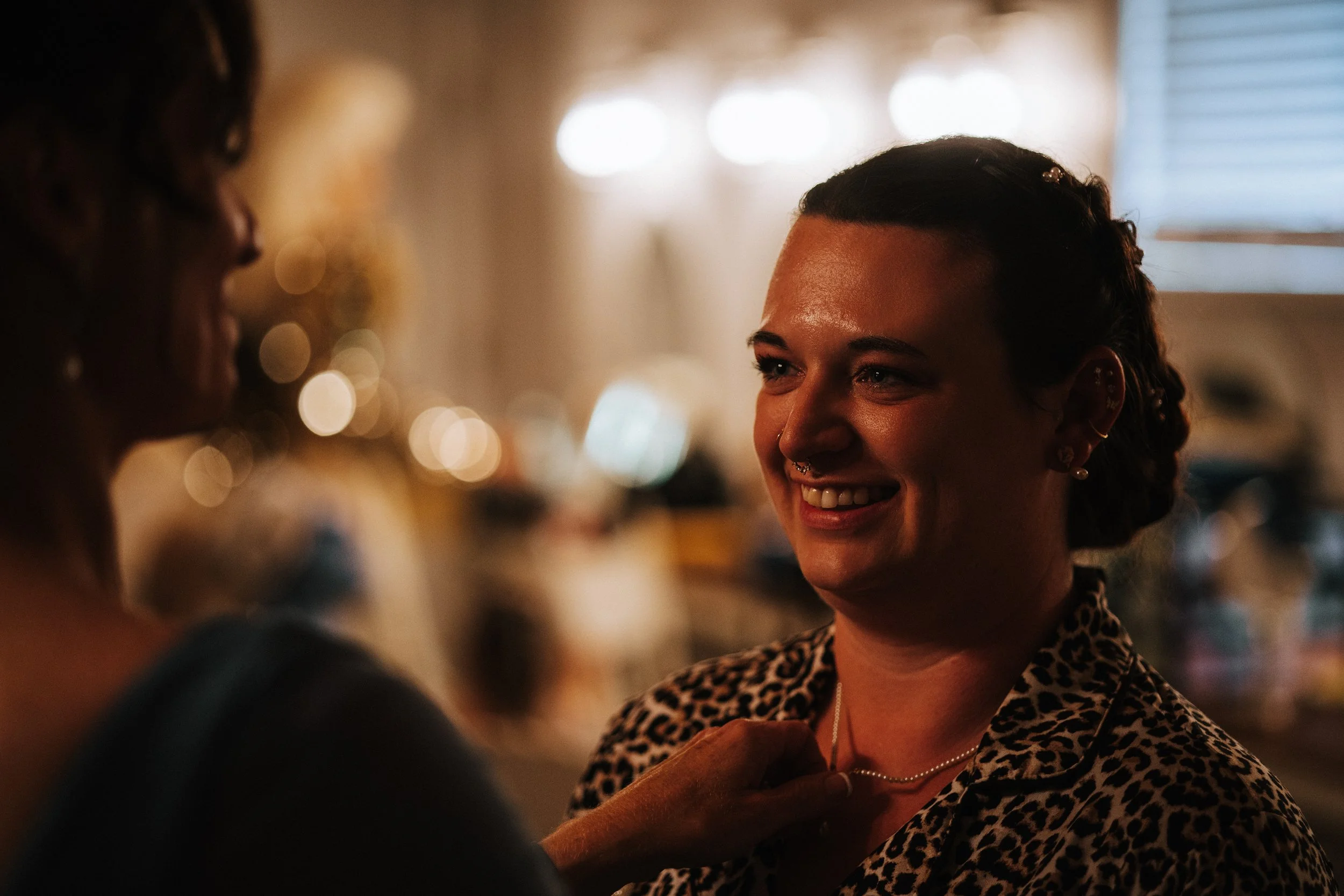 A woman smiling with braces and a leopard print jacket, talking to someone in a dimly lit indoor setting.