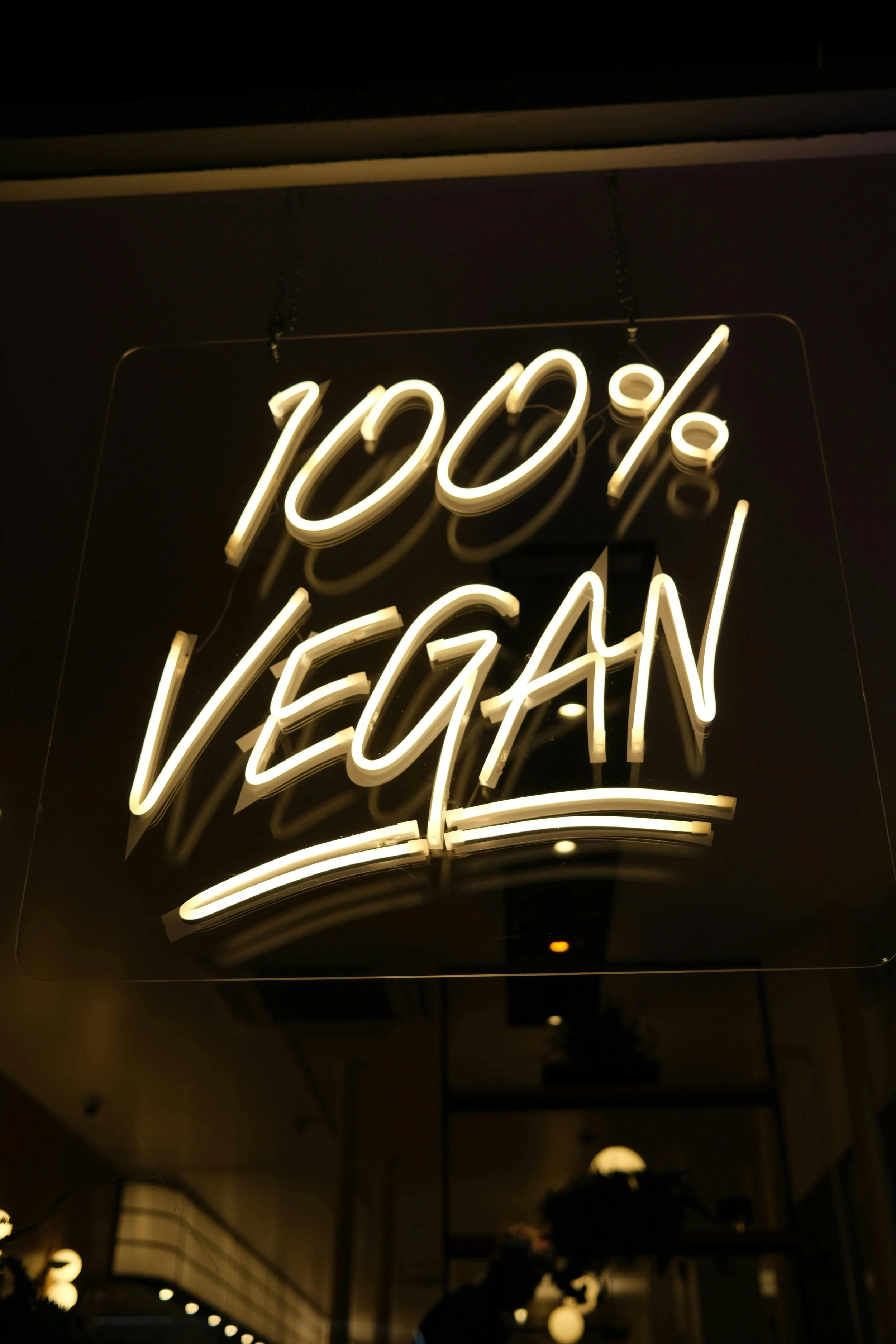 Neon sign displaying '100%' in warm light, hanging from ceiling in a dark indoor setting.