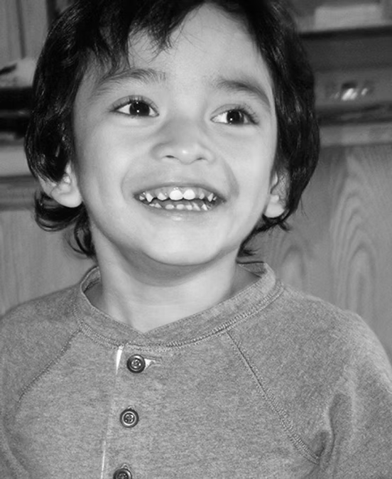 A young boy with dark hair smiling and showing missing front teeth in a black and white photo.