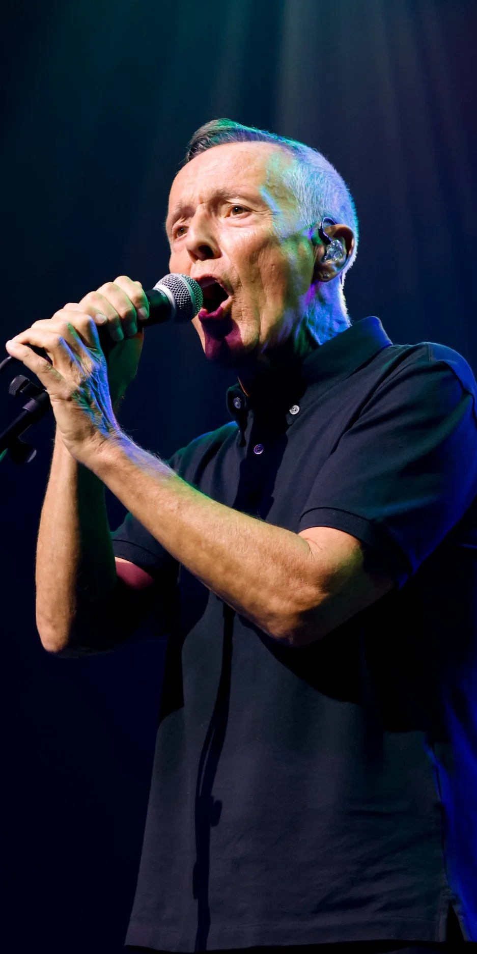 A man singing into a microphone on stage with colorful lighting.