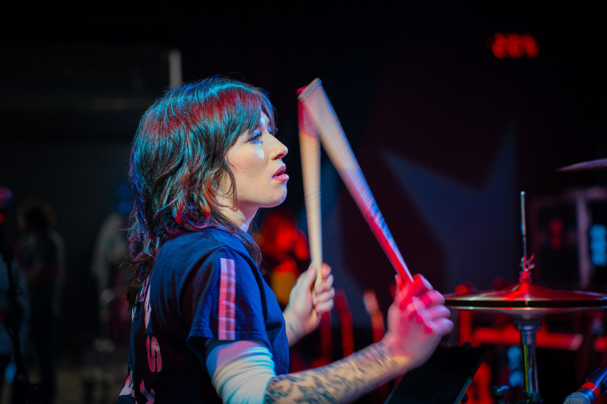 A woman with multi-colored hair playing drums in a darkened venue.
