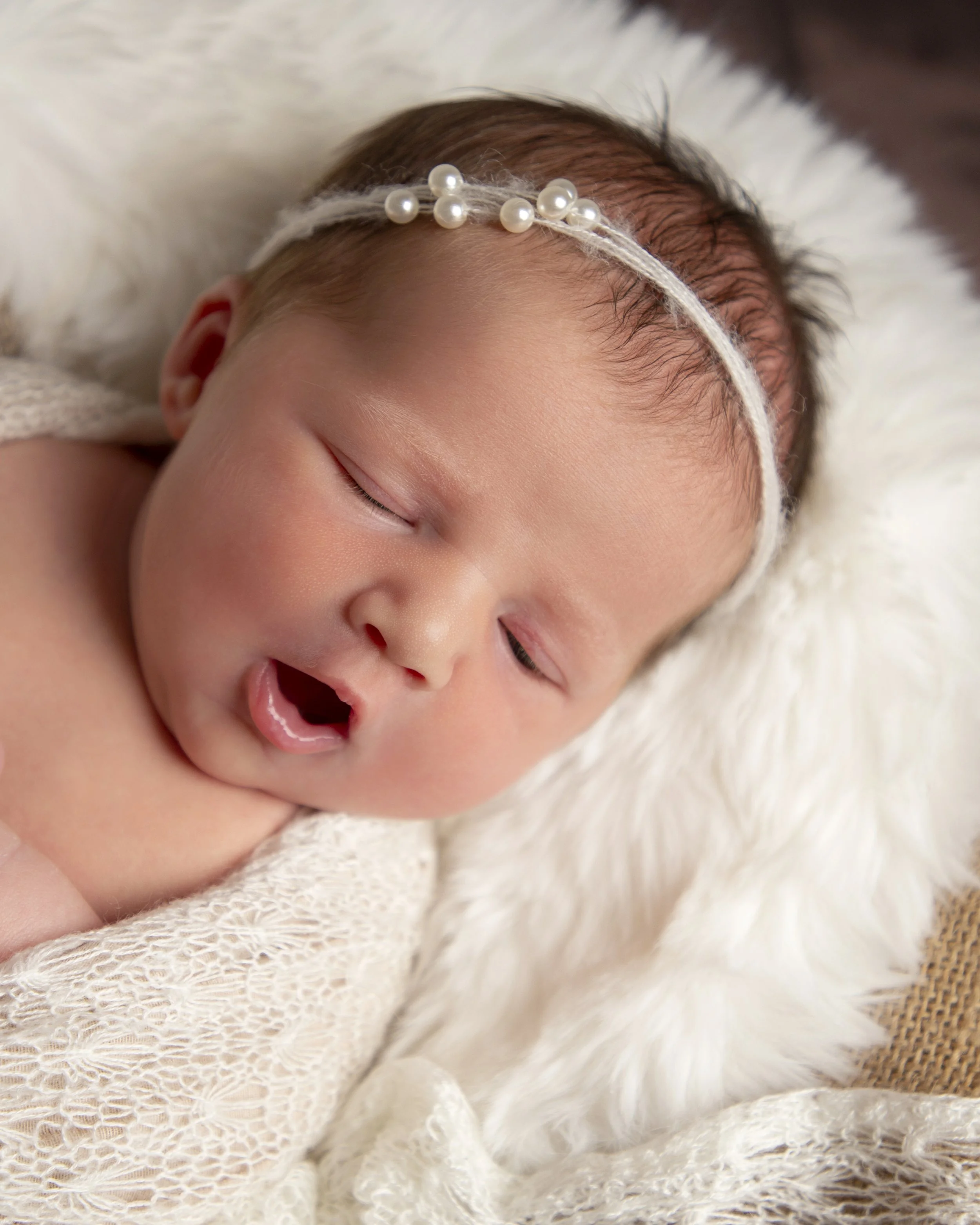 Close-up of a sleeping baby with a pearl headband, laying on a soft blanket.