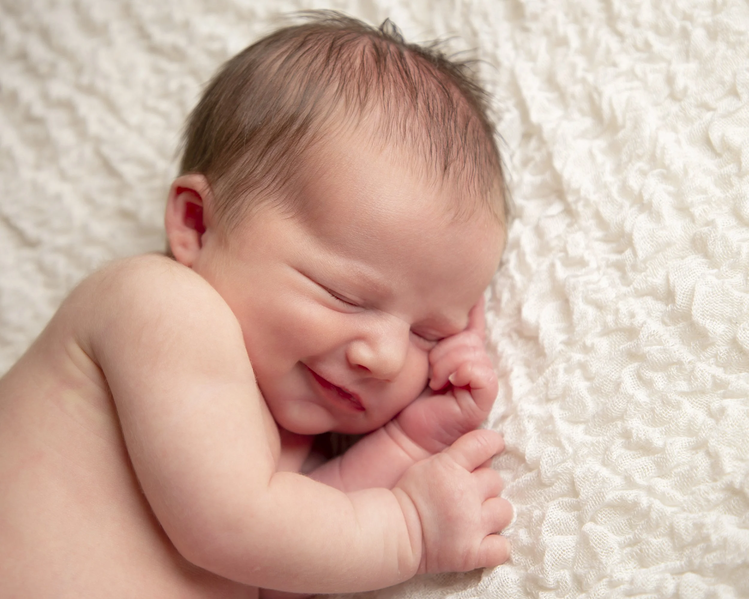 Close-up of a sleeping newborn baby with minimal hair, resting on a soft, textured white blanket.