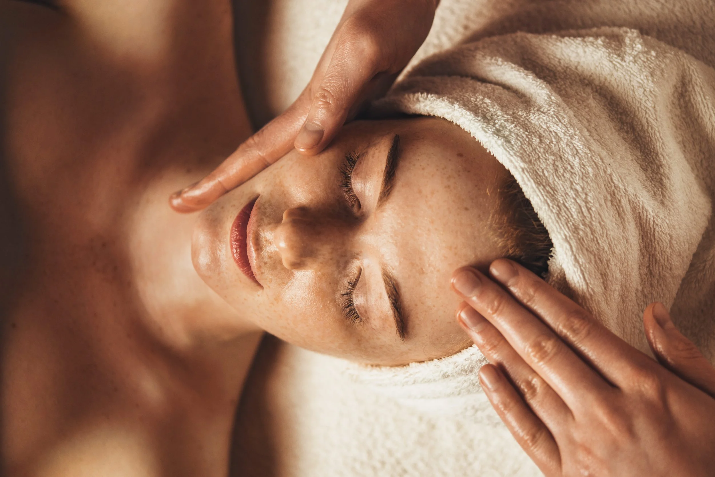 A person receiving a facial massage while lying down with a towel wrapped around their head.