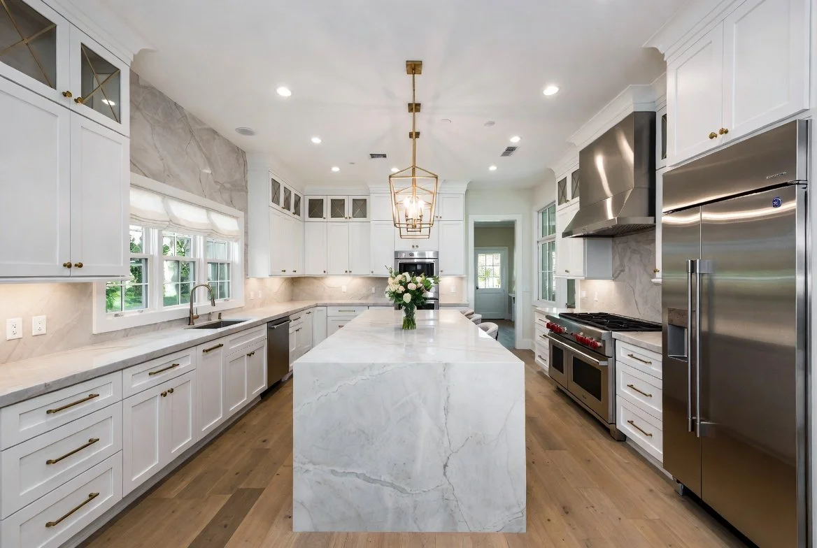 Modern kitchen with white cabinets, marble countertops, stainless steel appliances, and a large marble island with a flower vase in the center.