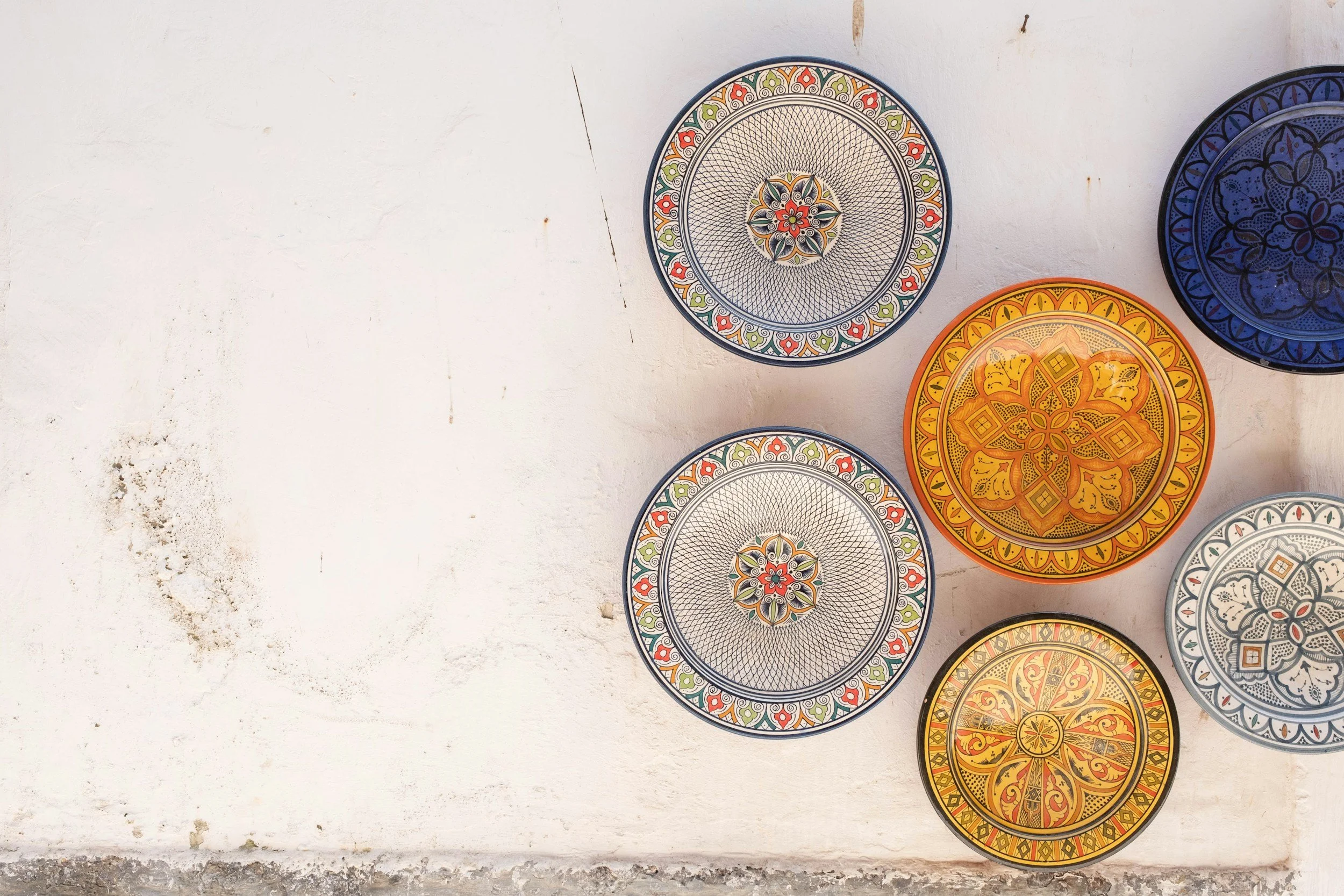 Colorful decorative ceramic plates with intricate patterns hanging on a white wall.
