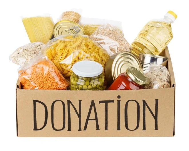 A cardboard box labeled 'Donation' filled with canned goods, pasta, rice, oil, and other nonperishable food items.