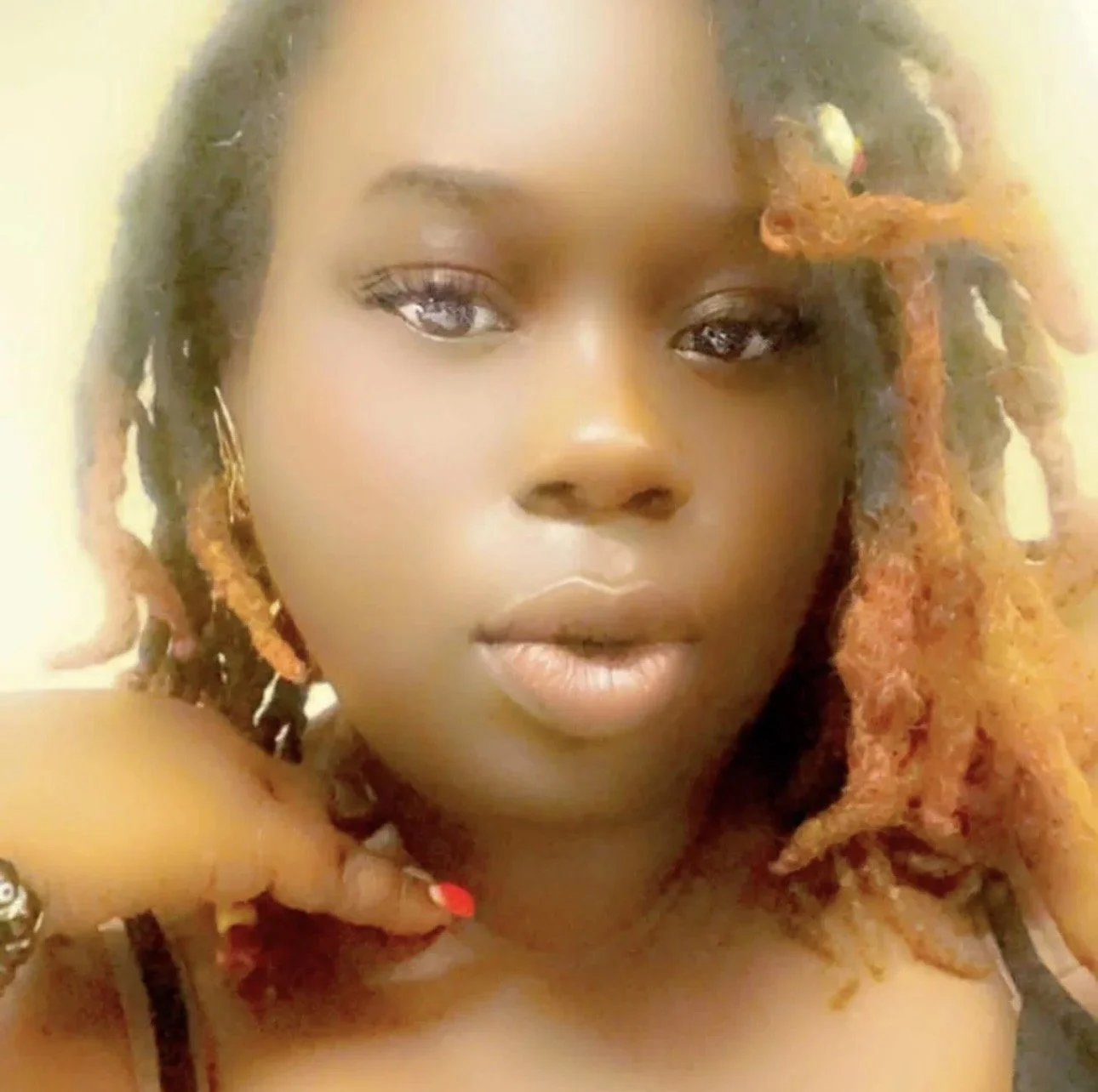 Close-up of a woman with dark skin and curly, orange-tinted hair looking into the camera.