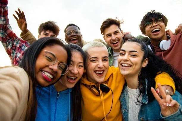 Group of diverse young people smiling and taking a selfie outdoors.