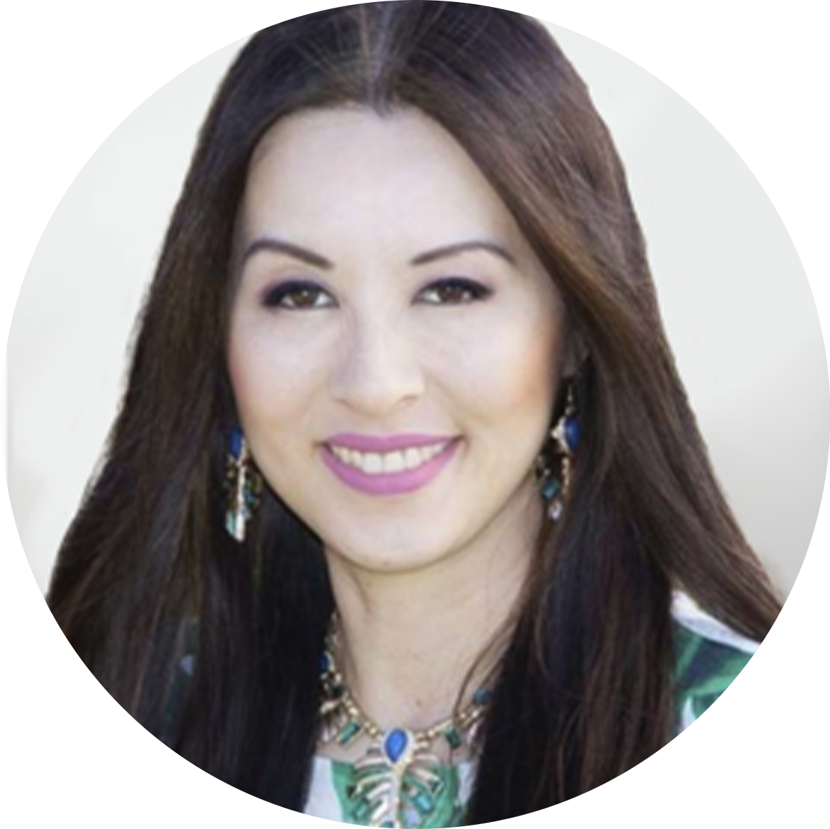 A smiling woman with long dark hair, wearing colorful jewelry including earrings and a necklace, against a blurred background.