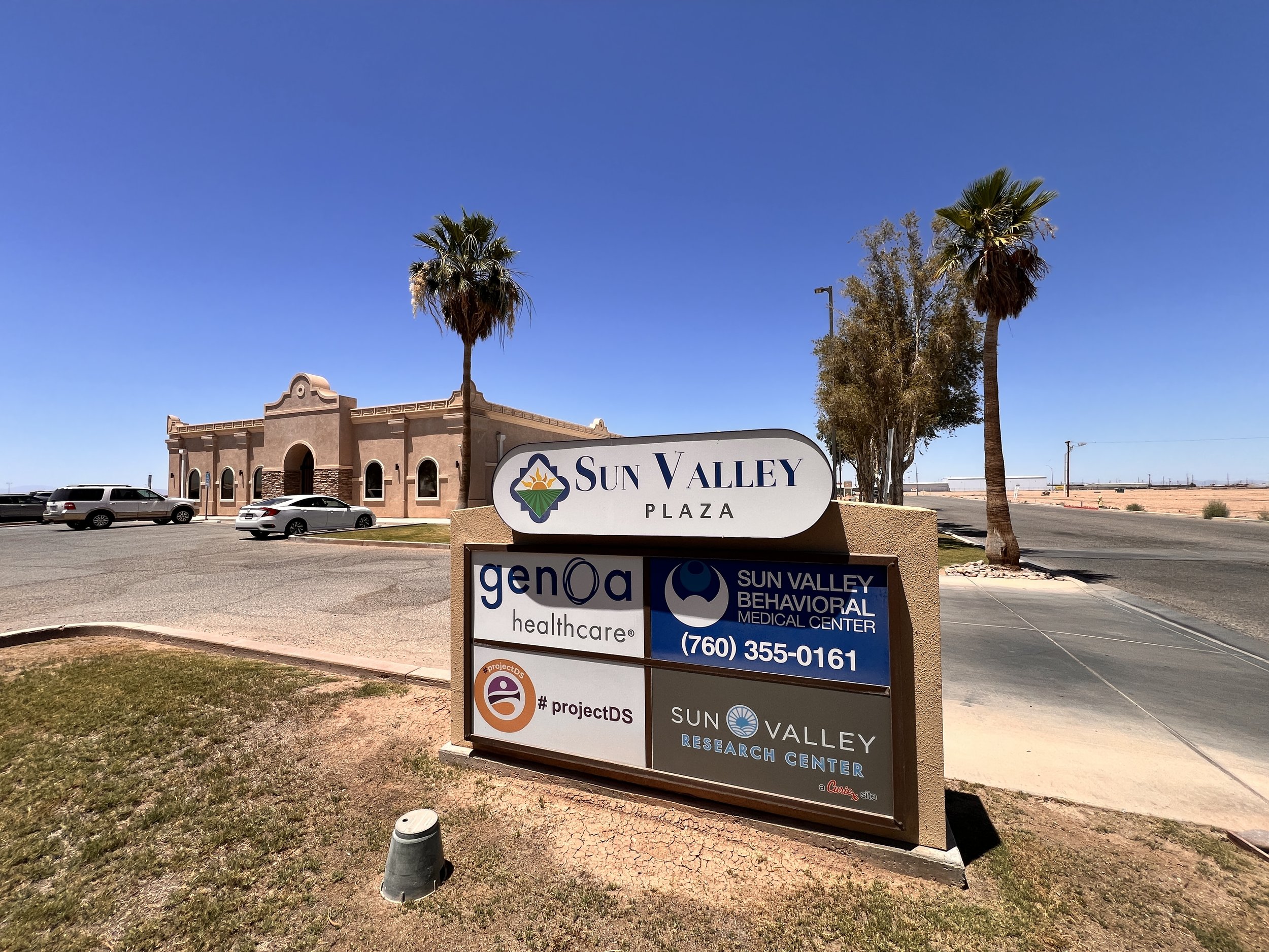 Sign for Sun Valley Plaza and associated medical and research centers, with parking lot and two palm trees in sunny, clear weather.