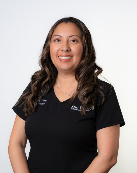 A woman with long, wavy brown hair smiling at the camera, wearing a black shirt with a logo and text.