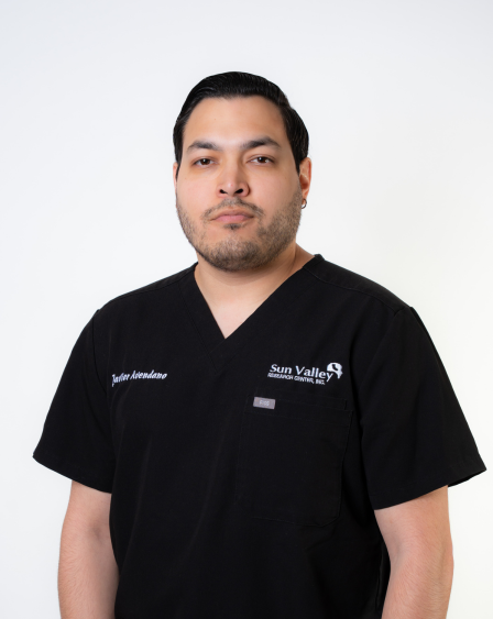 Professional portrait of a man in black medical scrubs with 'Sun Valley' and 'Juvie Alexandra' embroidered, standing against a white background.