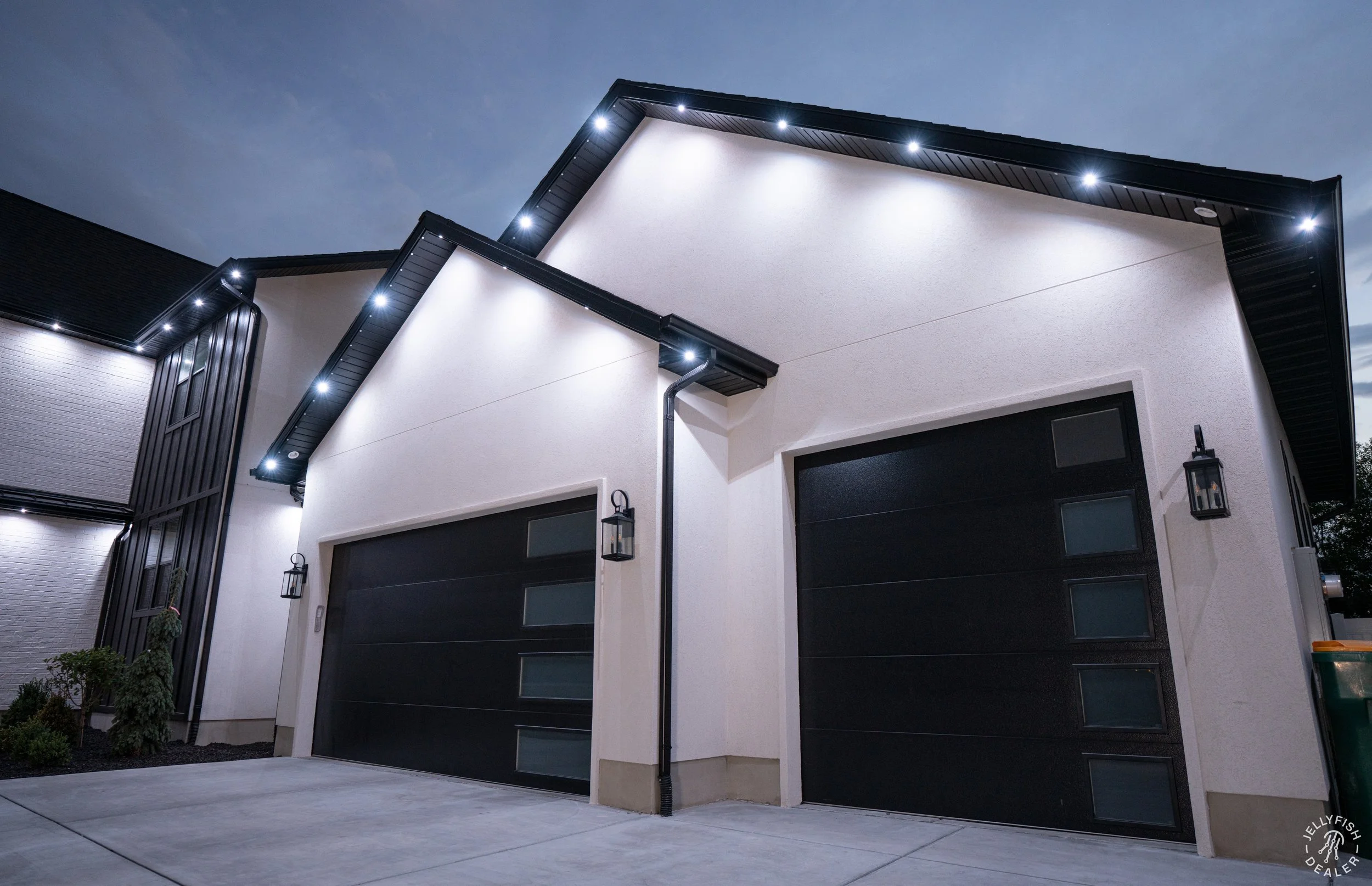 Modern house with black garage doors, exterior lighting, and minimal landscaping at night.