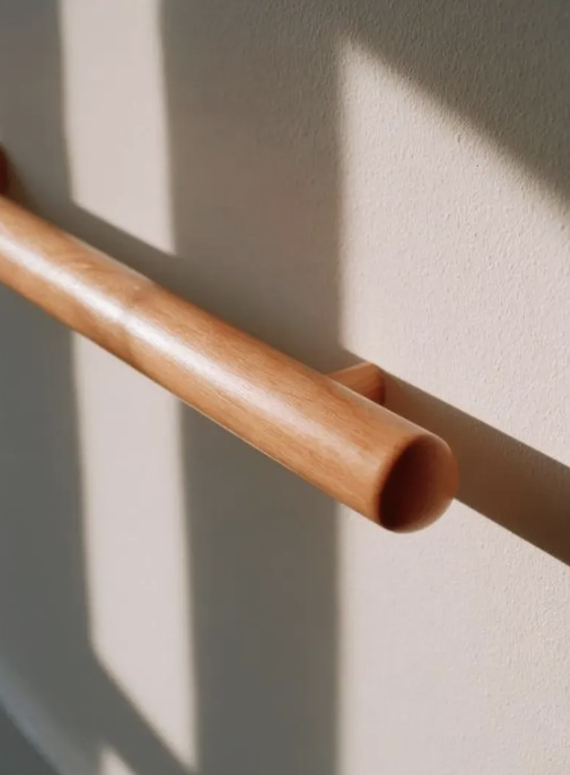 Close-up of a wooden handrail mounted on a beige wall with shadows cast on the wall.