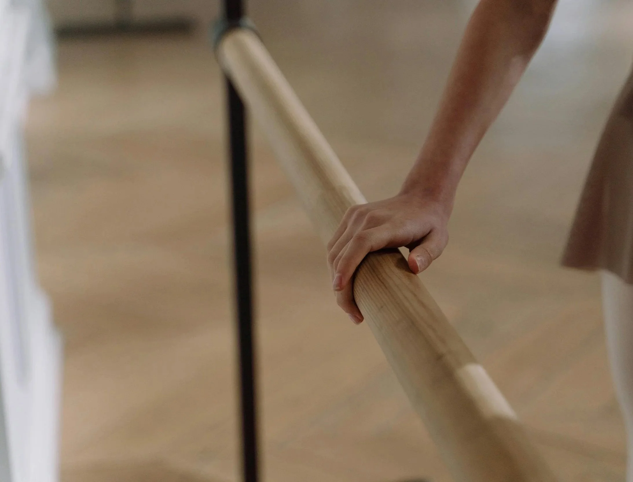 A person's hand gripping a wooden handrail on a staircase or ramp. The background is blurry.