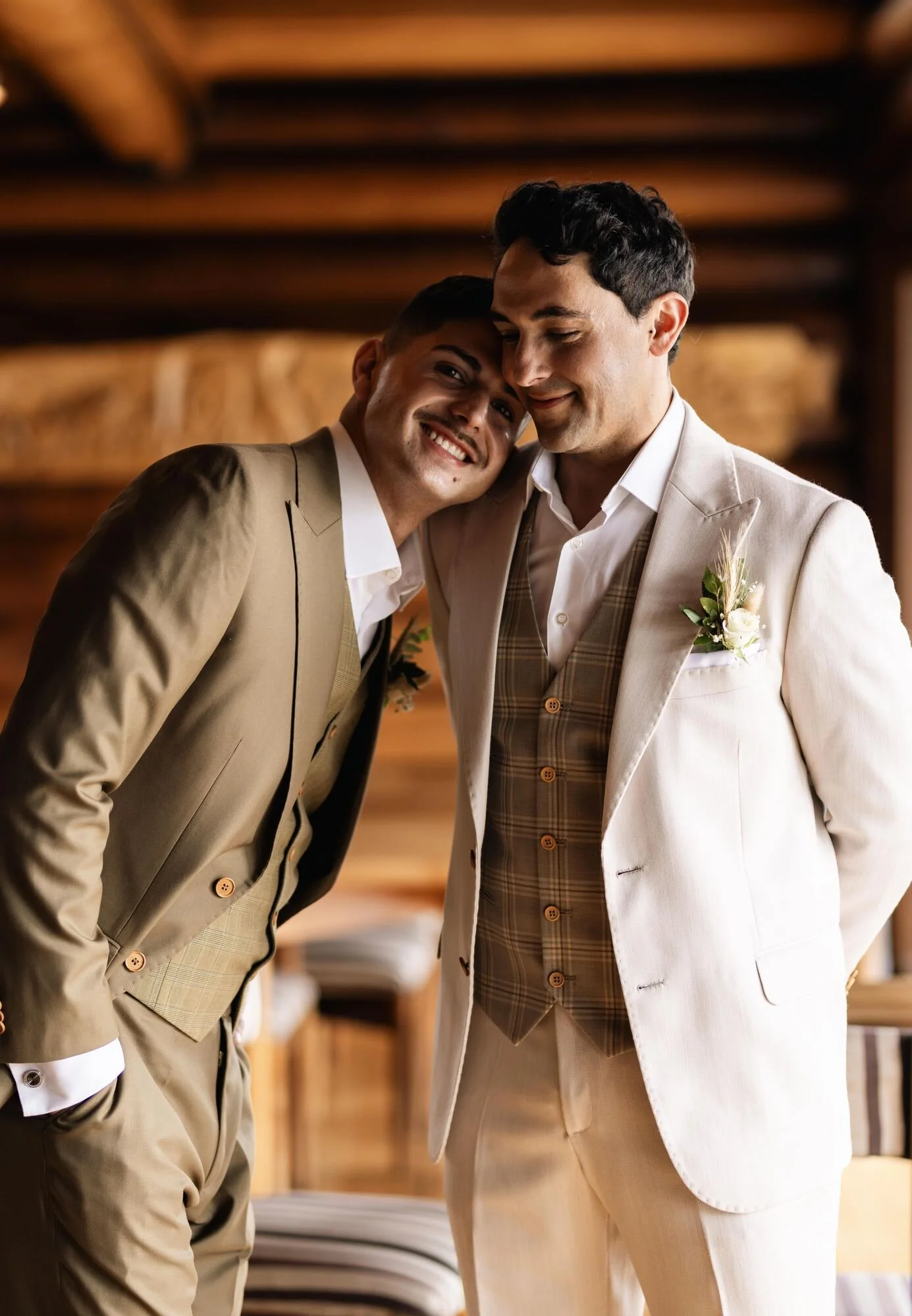 Los novios abrazados y riendo junto a una cabaña de madera en su boda igualitaria en Chiloé