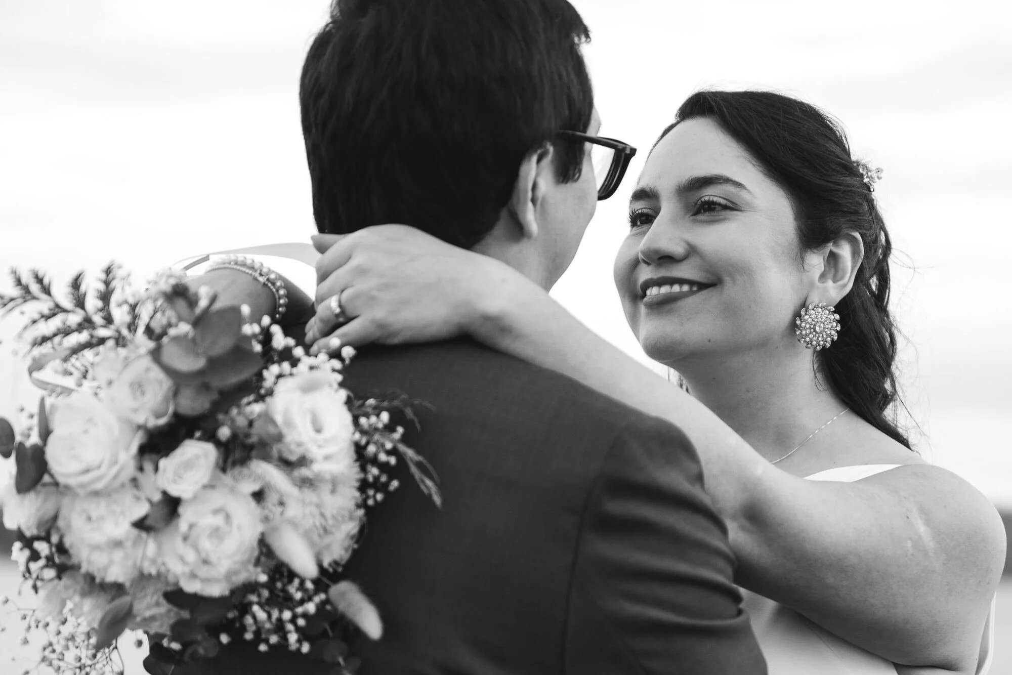La novia abraza al novio sosteniendo su ramo, en blanco y negro, Castro, Chiloé	