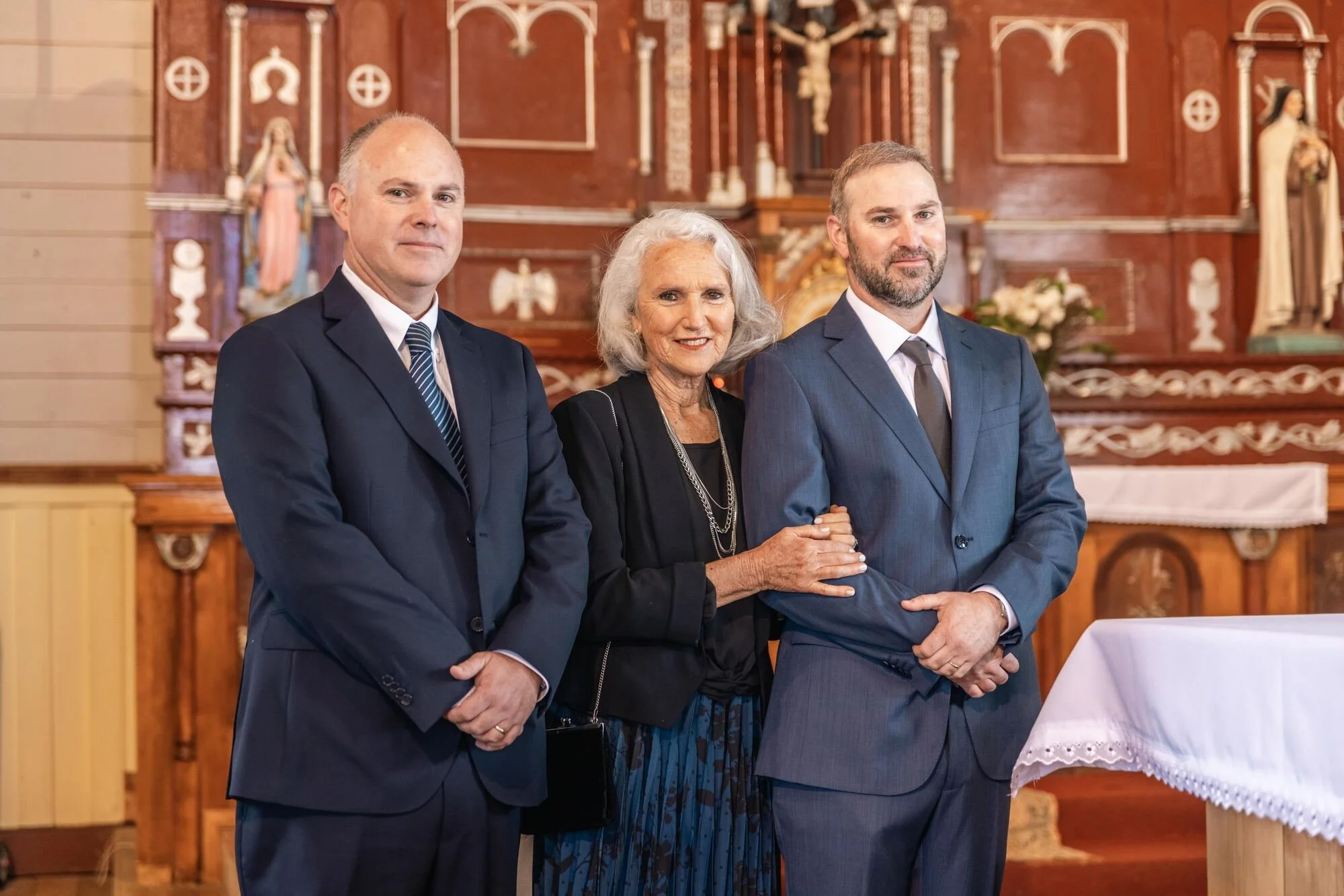 El novio junto a sus padres en el altar de la iglesia, boda en Chiloé	