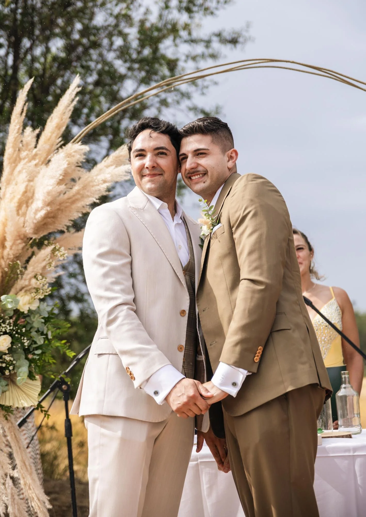 Retrato de los novios tomados de la mano bajo el arco de pampas en Ancud, Chiloé
