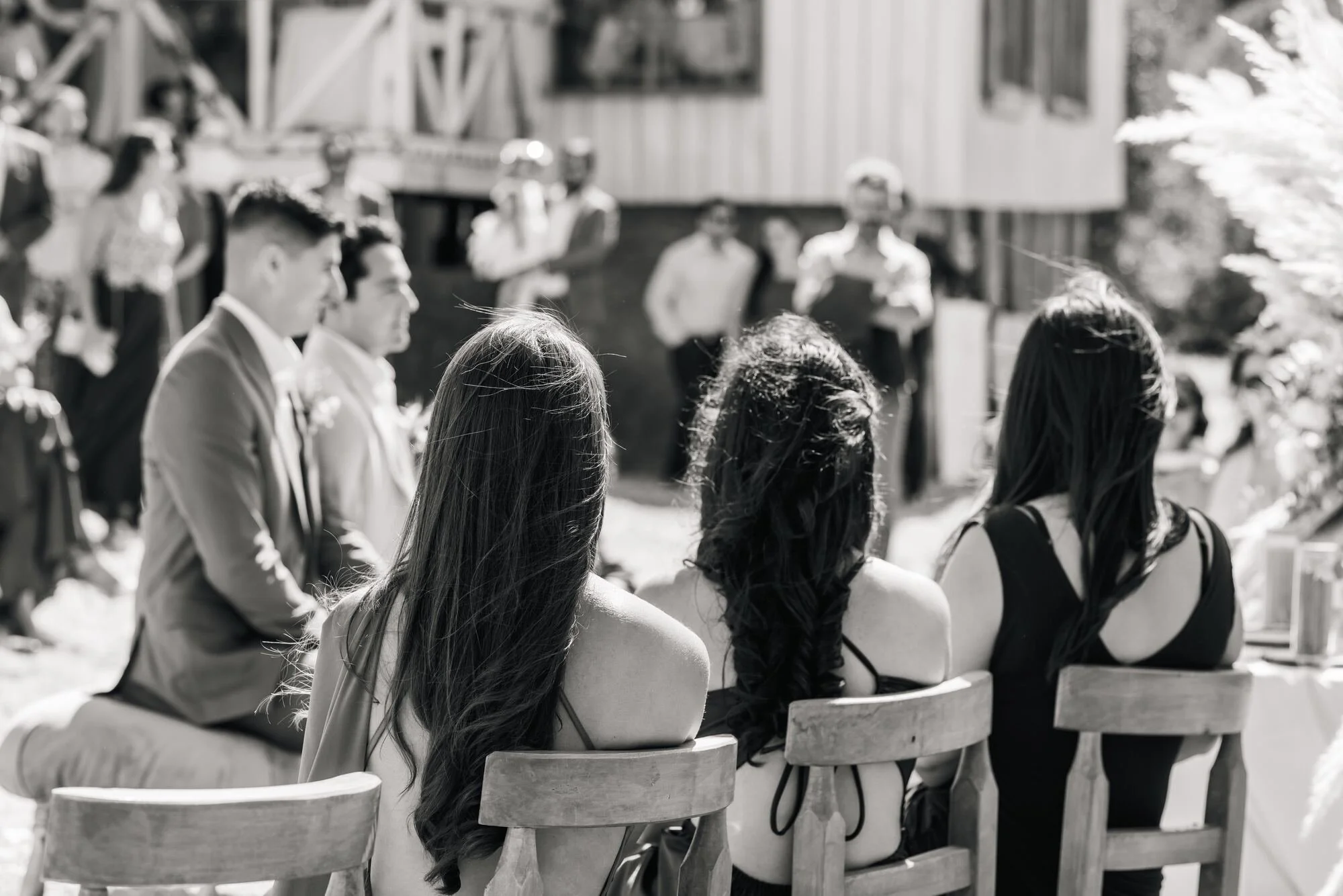 Ceremonia de matrimonio al aire libre junto a una construcción de madera chilota, en blanco y negro, Ancud