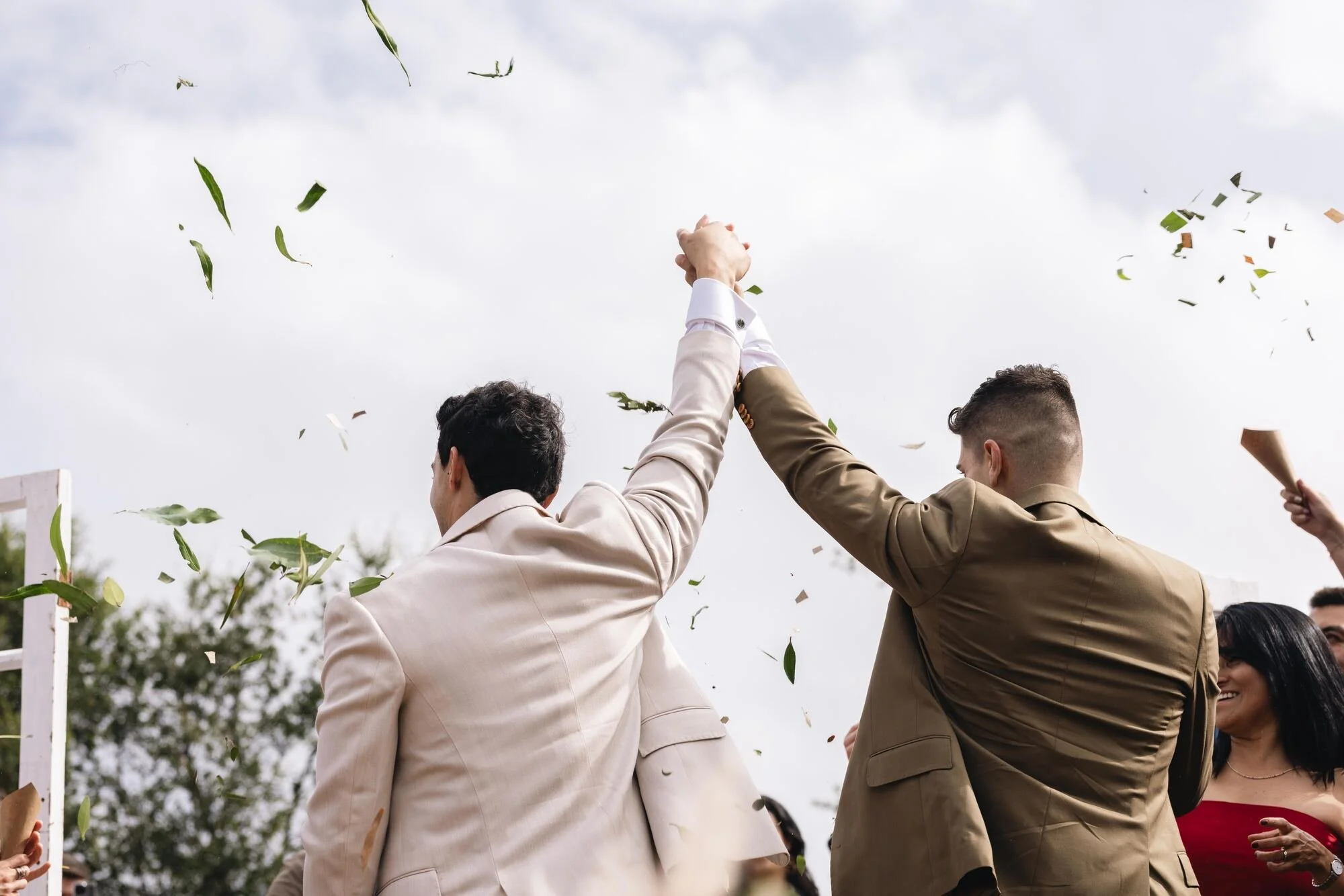Los novios levantan las manos en señal de celebración bajo la lluvia de hojas, boda campestre en Ancud