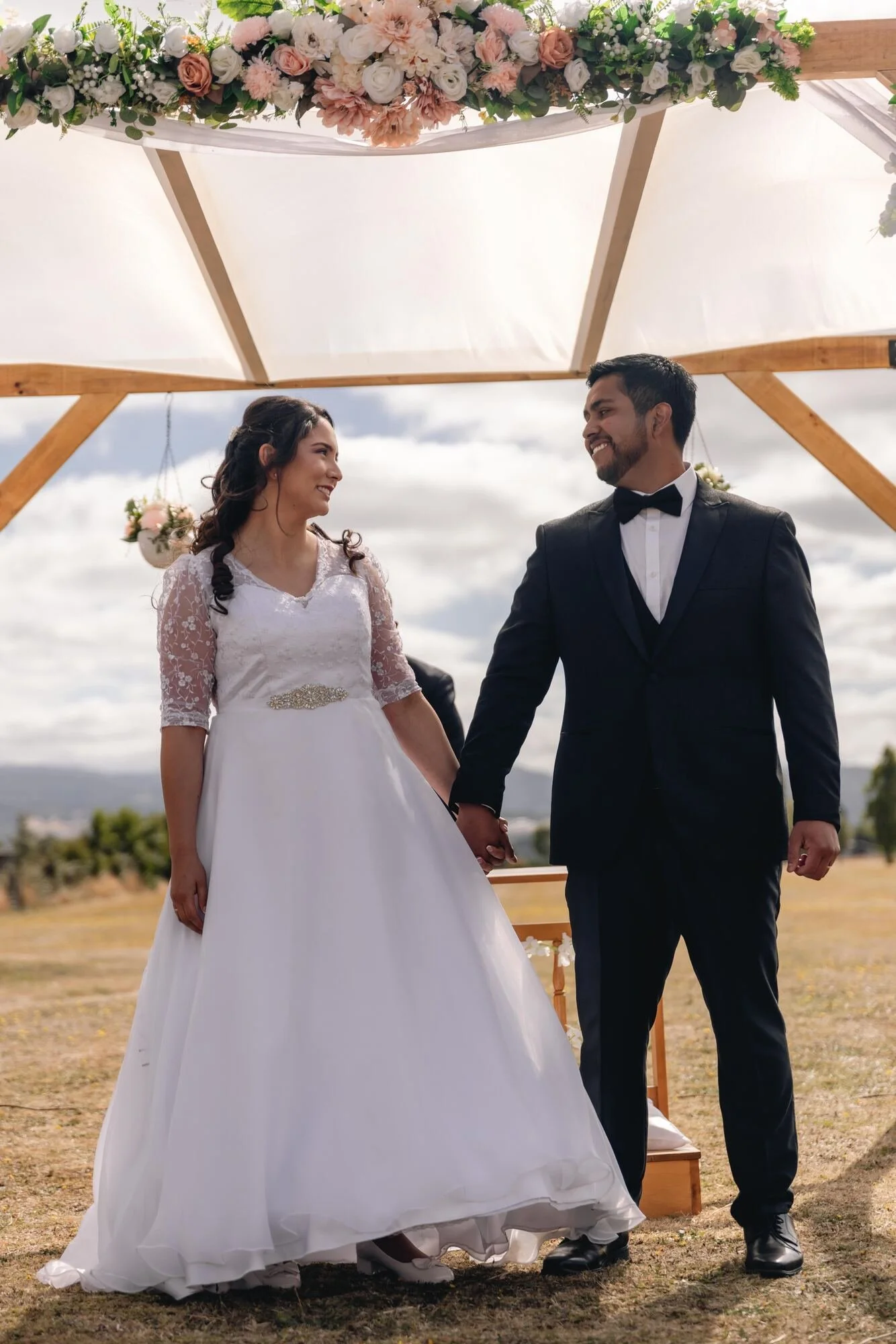 Los novios tomados de la mano bajo el arco floral en Quilquico, Castro, Chiloé	