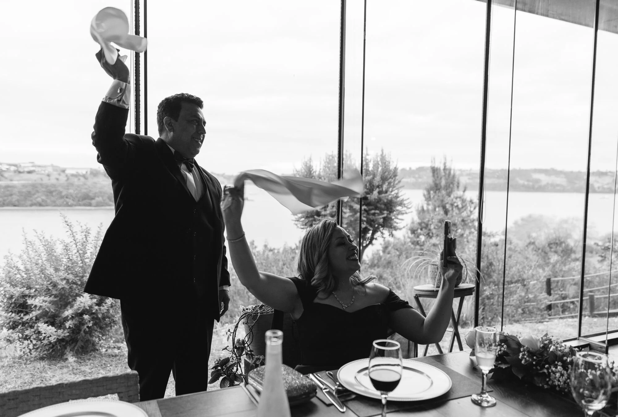 Invitados celebrando con servilletas en alto, en blanco y negro, boda en Castro, Chiloé