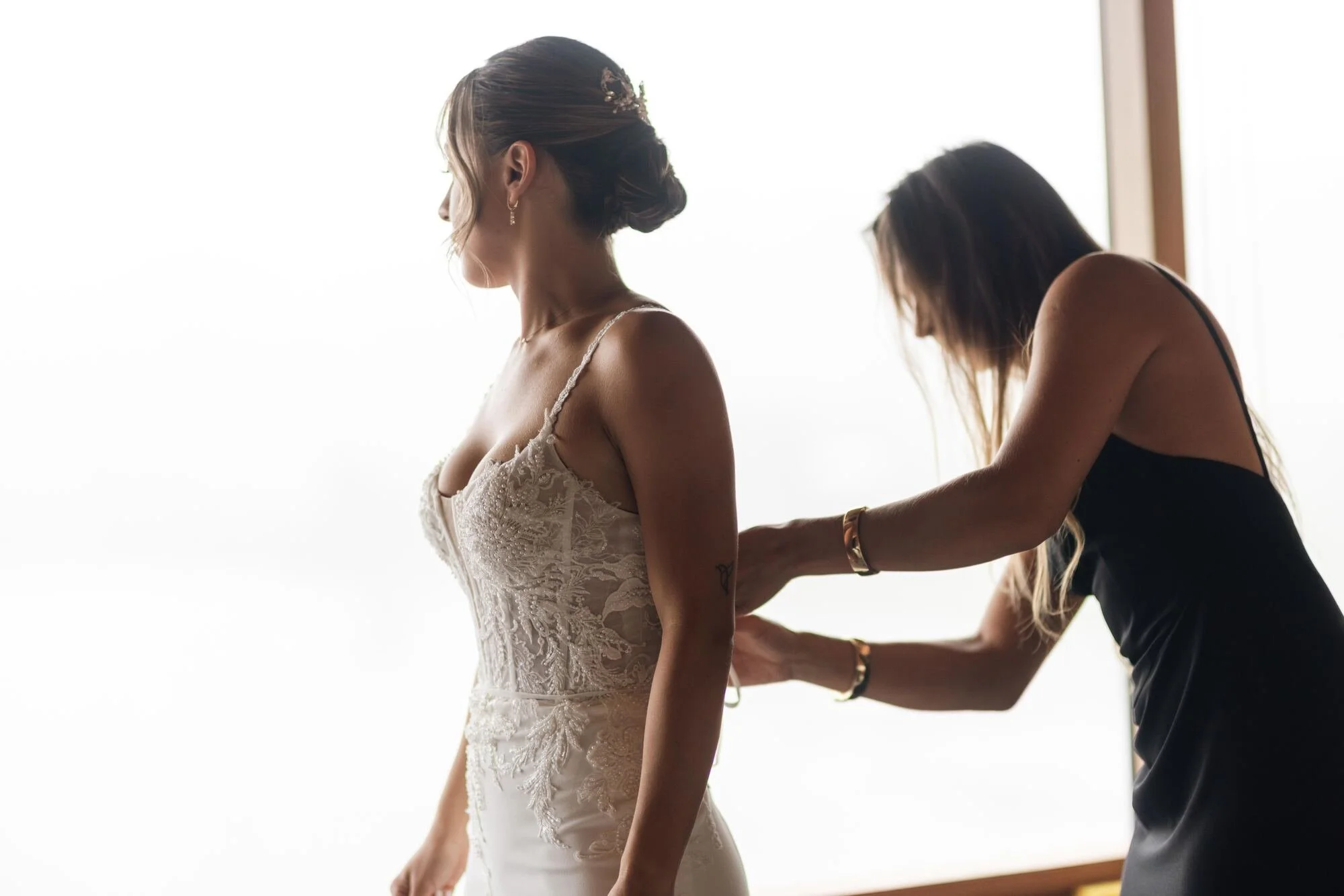 Ajustando el vestido de la novia junto al ventanal en Refugia, Castro, Chiloé