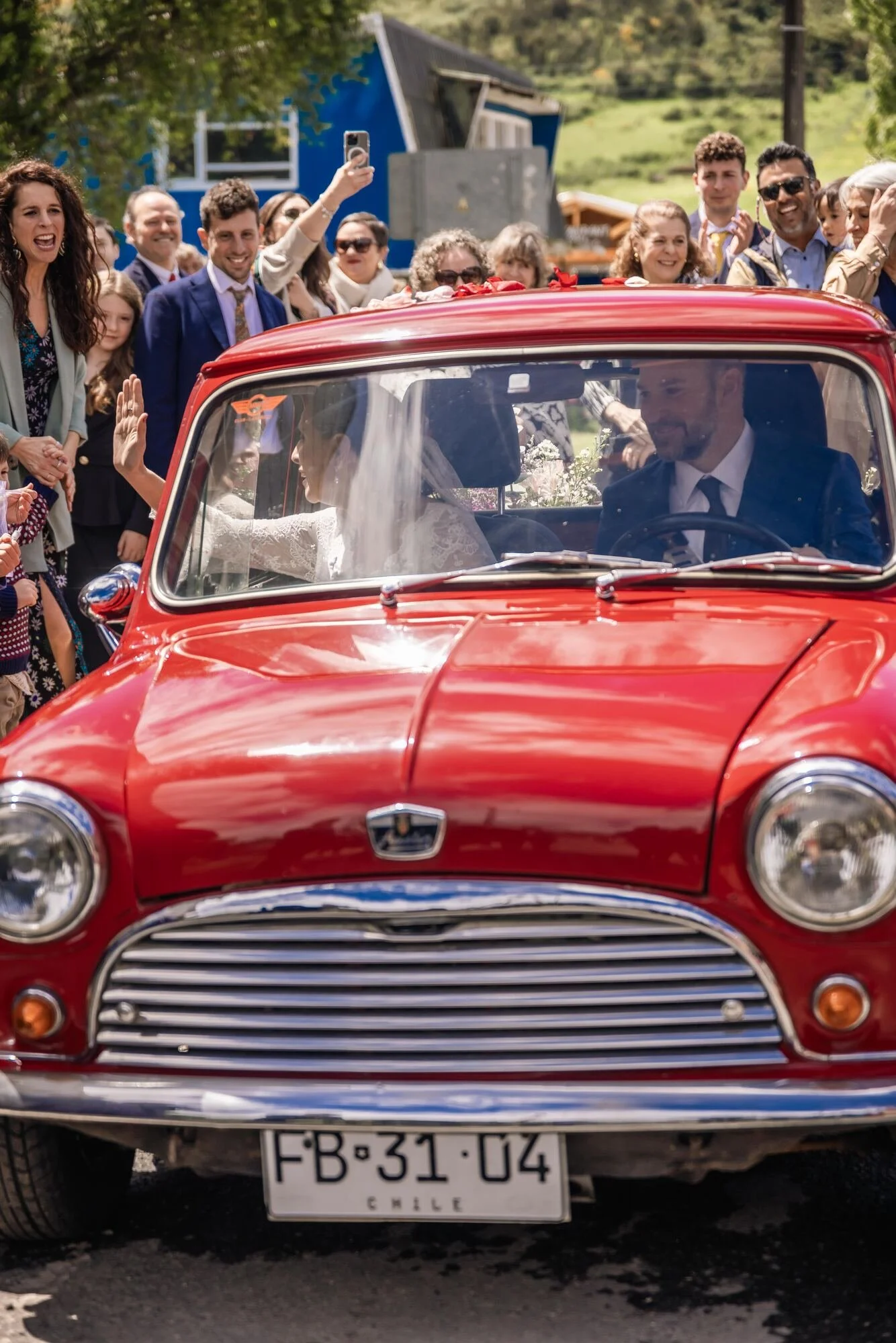 Auto clásico rojo con los novios a bordo rodeado de invitados, Castro, Chiloé	