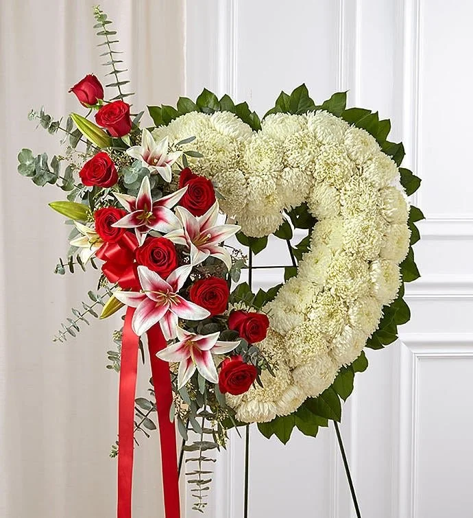 A floral wreath with white chrysanthemums, red roses, and pink lilies, decorated with green eucalyptus and accented by a red ribbon.