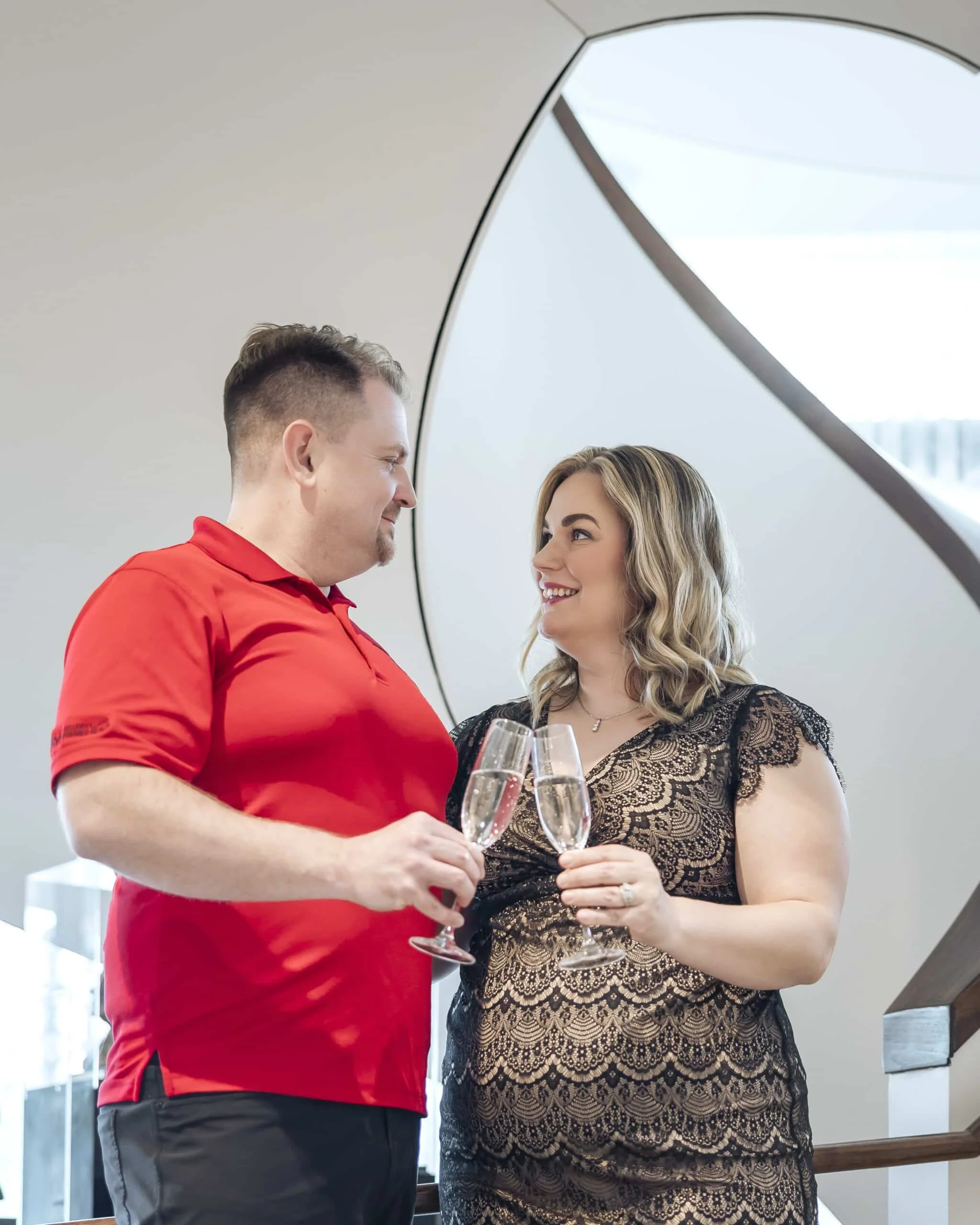 A man and a woman holding champagne glasses and looking at each other during a celebration or special occasion in a modern setting.