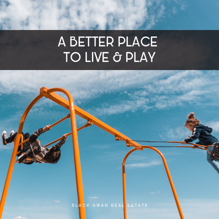 Two children playing on a swing set outdoors under a blue sky with clouds