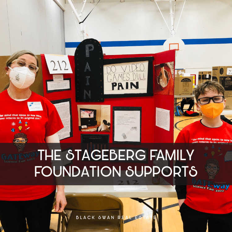 A woman and a boy wearing red shirts with 'Gateway Science Fair 2022' logo, standing next to an academic project display board titled 'Pain', with a sign that says 'Do video games dull pain'. They are in a gymnasium with other project displays visible in the background. Both are wearing face masks.