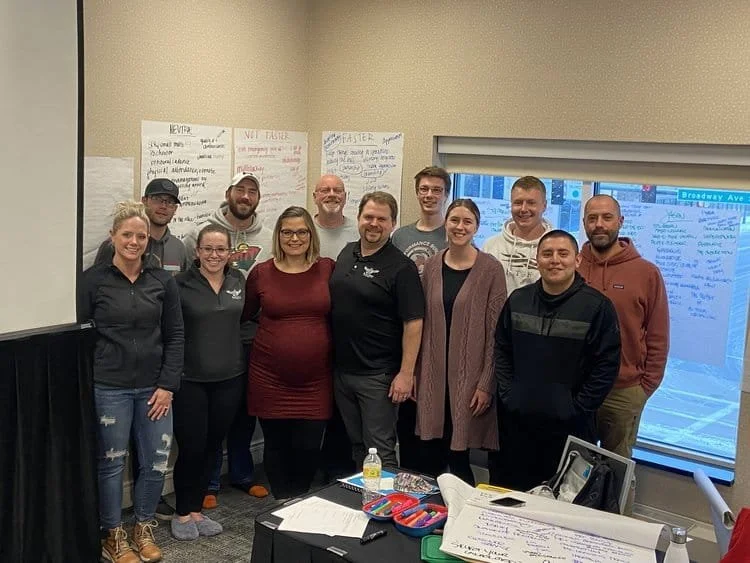 Group of ten people posing for a photo in a conference room with whiteboards and notes on the wall.