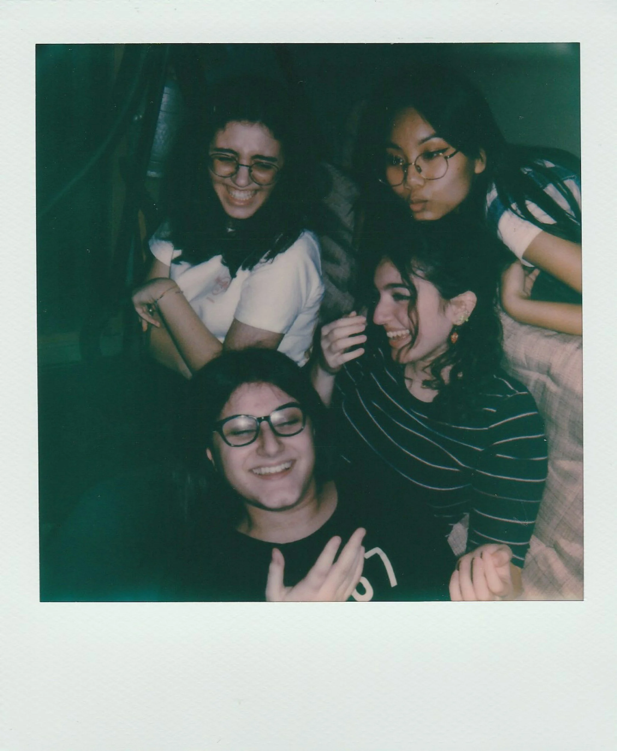 Three women smiling and laughing together, wearing glasses, in a casual setting with one woman wearing a striped shirt.