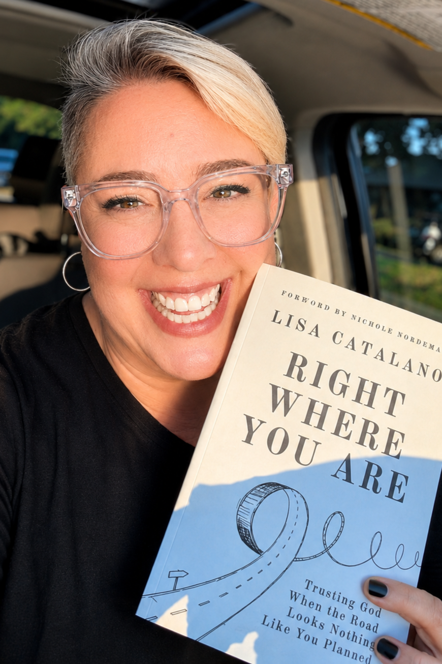 Lisa Catalano smiling with short, platinum blonde hair and glasses, holding her first copy of her book titled 'Right Where You Are'  inside a vehicle.