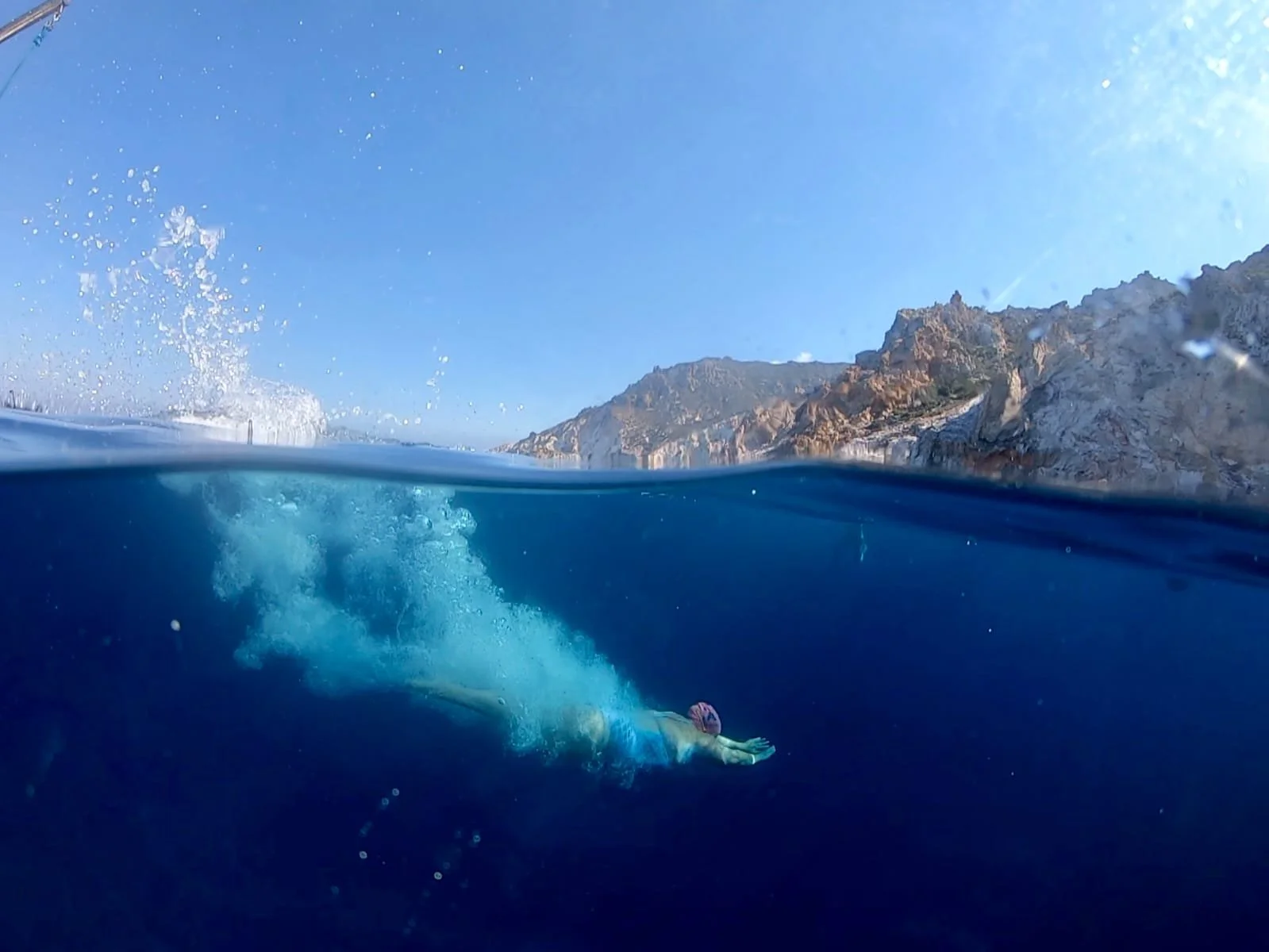 Swimmer floating in the ocean near rocky cliffs under a clear blue sky.