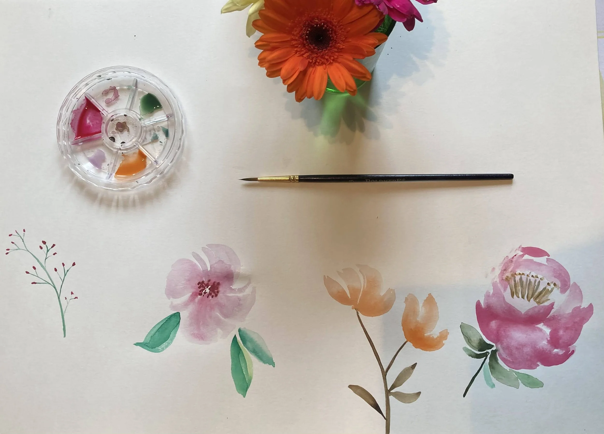 Watercolor floral pattern on paper with pink, red, orange, and green flowers and leaves. A black-handled paintbrush and a small palette with pink, green, and orange paint are placed on top of the pattern.
