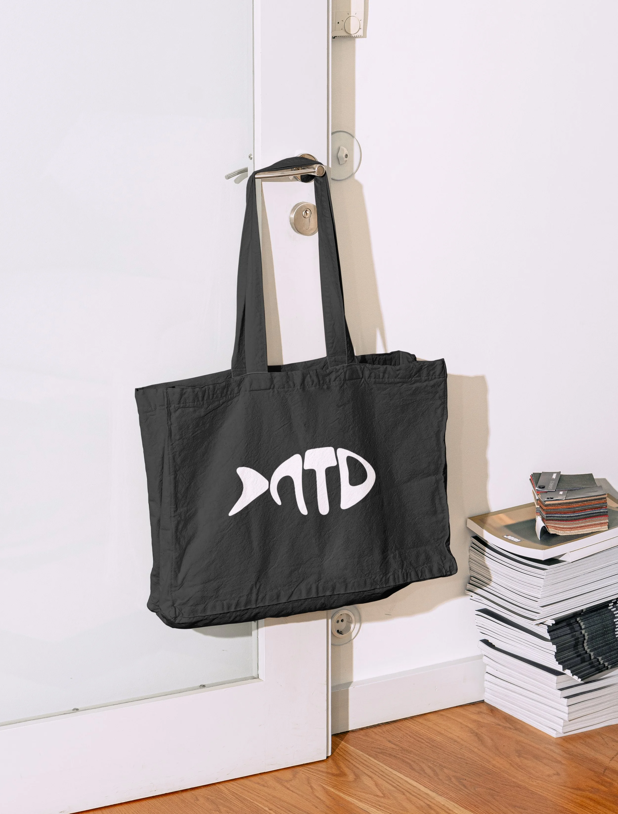 Not That Deep tote bag with 3D fish logo next to a stack of magazines
