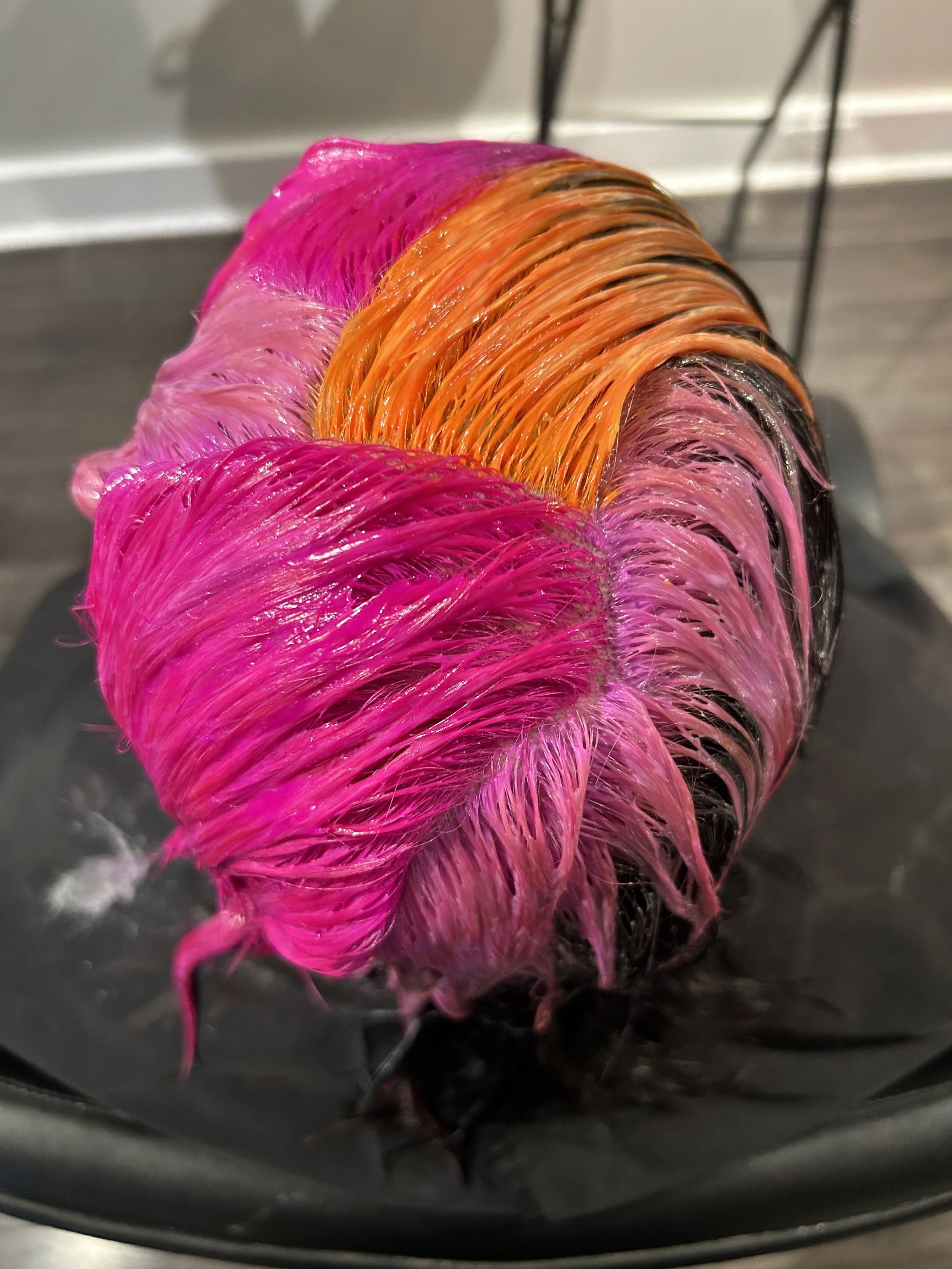 Close-up of wet, colorful hair in shades of pink, orange, and blonde, lying on a black surface.