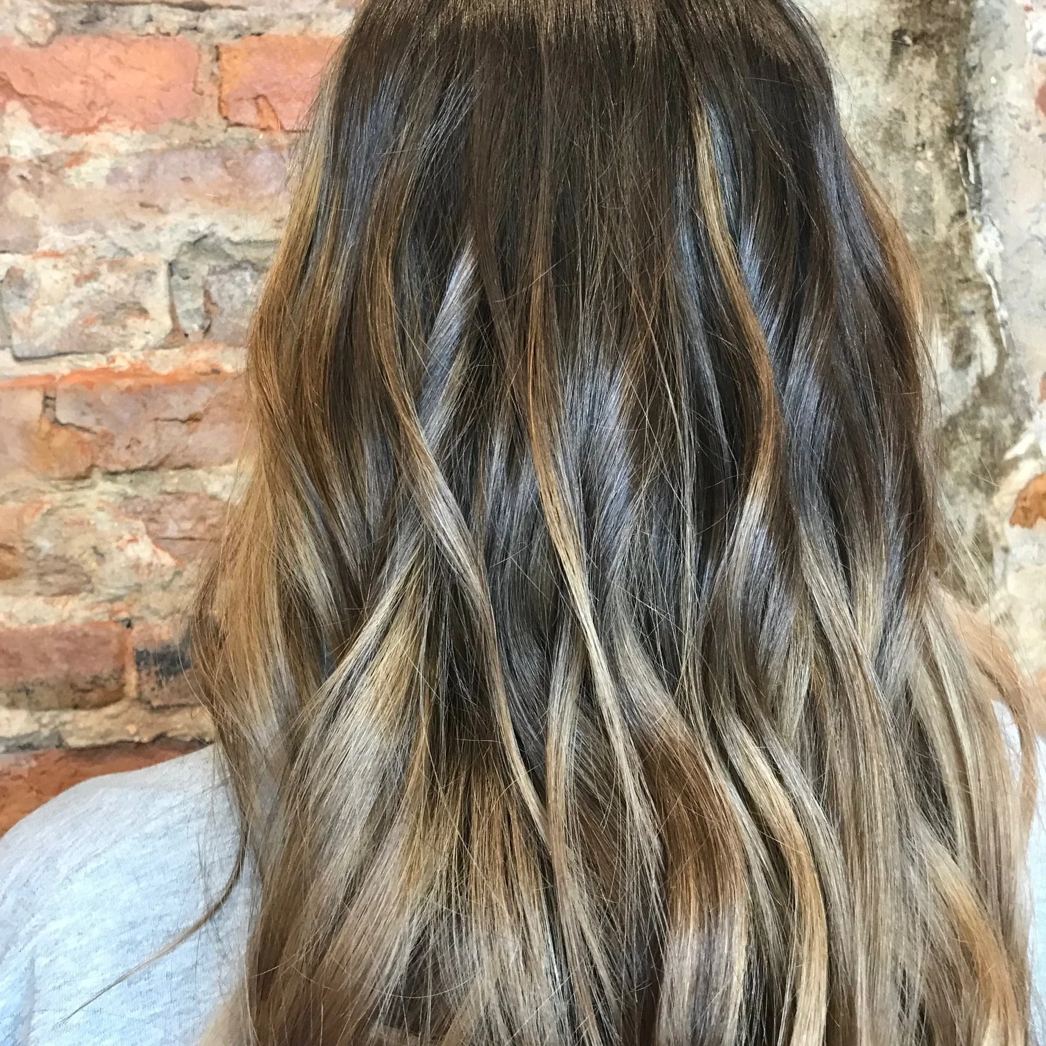 Close-up of a woman's wavy, highlighting hair with blonde highlights against a brick wall background.