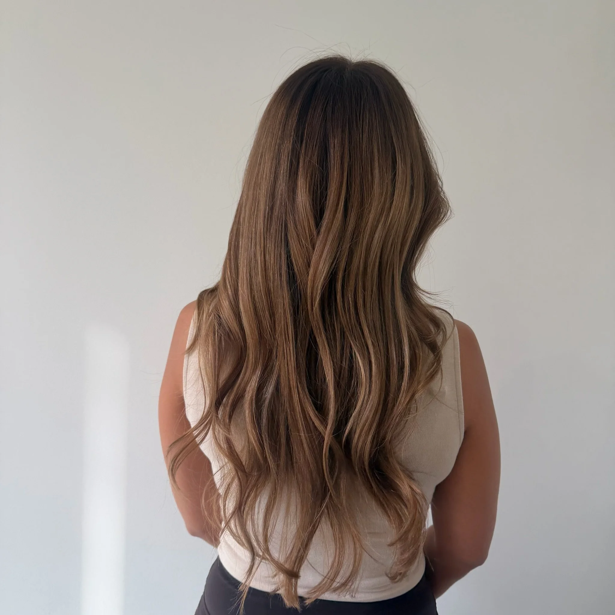 Close-up of a woman's wavy, highlighted hair with blonde highlights against a brick wall background.