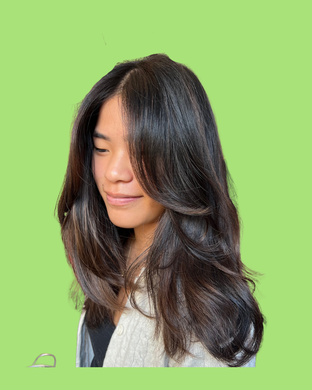 Portrait of a woman with dark, wavy hair, looking downward with a slight smile, against a bright green background.